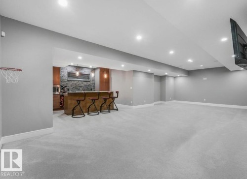 Expansive lower-level space featuring recessed lighting, light-colored carpeting, a built-in wet bar with stone-finish backsplash, and pendant lighting - 8927 120 Street Nw, Edmonton, AB - Indoor