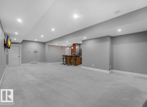 Recessed lighting illuminates the expansive carpeted area with a built-in wet bar featuring wood cabinetry and a tiled backsplash - 8927 120 Street Nw, Edmonton, AB - Indoor