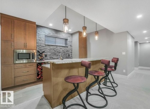 Built-in wet bar with wood cabinetry, stainless steel microwave, stone accent wall, and recessed lighting - 8927 120 Street Nw, Edmonton, AB - Indoor Photo Showing Kitchen