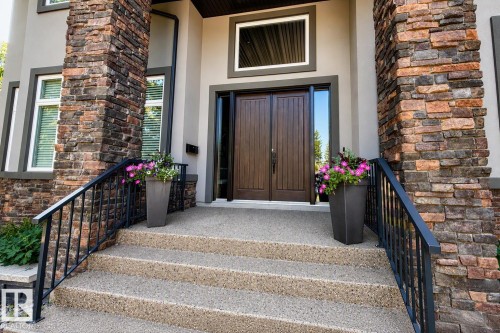Double front doors with vertical wood paneling, flanked by decorative stone columns, and an exposed aggregate concrete staircase with black metal railings - 8927 120 Street Nw, Edmonton, AB - Outdoor