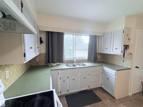 Kitchen featuring white cabinetry, a green countertop, and a decorative tile backsplash - 5411 44 Ave, Wetaskiwin, AB - Indoor Photo Showing Kitchen With Double Sink