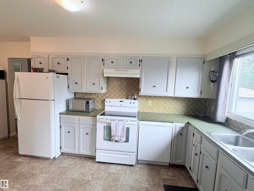 Kitchen featuring white cabinetry, green countertops, and a patterned backsplash - 5411 44 Ave, Wetaskiwin, AB - Indoor Photo Showing Kitchen