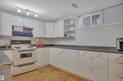Kitchen featuring extensive white cabinetry, wood-finish flooring, a built-in range, dark countertops, and a window with blinds - 