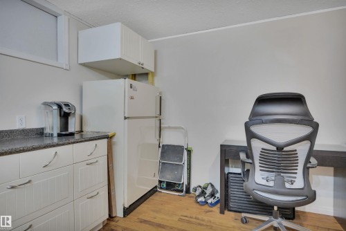 Compact kitchen area featuring white cabinetry with brushed nickel pulls, a speckled dark countertop, and a white refrigerator - 5411 44 Ave, Wetaskiwin, AB - Indoor
