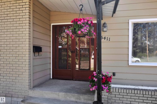 Exterior featuring tan horizontal siding, light brick accents, a dark wood-finish double entry door with glass panels, and a concrete stoop - 5411 44 Ave, Wetaskiwin, AB - Outdoor With Exterior