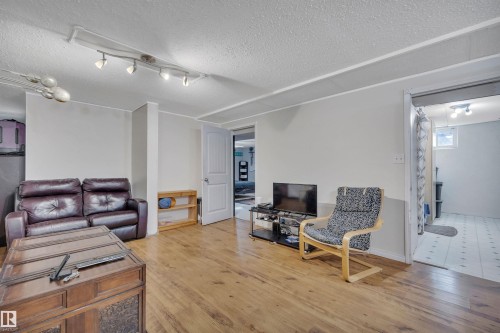 Spacious room featuring wood-finish flooring, track lighting, light gray walls, and a white paneled door - 5411 44 Ave, Wetaskiwin, AB - Indoor