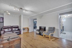 Spacious room featuring wood-finish flooring, track lighting, light gray walls, and a white paneled door - 