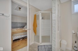 Corner shower enclosure with clear and frosted glass panels, light-toned walls, a small high window, and wood-finish flooring visible through an open doorway - 