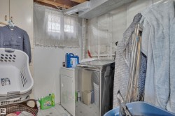 Laundry area with a window featuring lace curtains, exposed ceiling joists, and a visible dryer vent - 