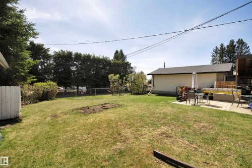 Expansive rear yard featuring a concrete patio, mature perimeter trees, and a detached structure with a pitched roof - 5411 44 Ave, Wetaskiwin, AB - Outdoor
