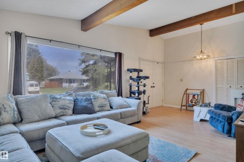 Living area featuring expansive picture window, wood-finish flooring, vaulted ceilings, exposed ceiling beams, and a ceiling-mounted light fixture - 5411 44 Ave, Wetaskiwin, AB - Indoor Photo Showing Living Room