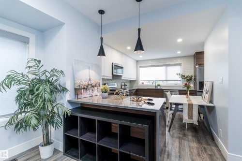Modern kitchen featuring wood-finish flooring, two-tone cabinetry, stainless steel appliances, and a tiled backsplash - 10934 80 Avenue Nw, Edmonton, AB - Indoor Photo Showing Other Room