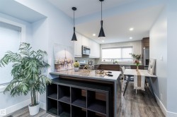 Modern kitchen featuring wood-finish flooring, two-tone cabinetry, stainless steel appliances, and a tiled backsplash - 