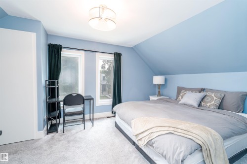 Sloped ceiling room featuring two windows with dark curtains, a built-in wall niche, and light-colored carpeting - 10934 80 Avenue Nw, Edmonton, AB - Indoor Photo Showing Bedroom