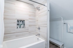 Bathtub and shower combination featuring large format neutral-toned wall tiles with a recessed niche accented by mosaic tiling - 