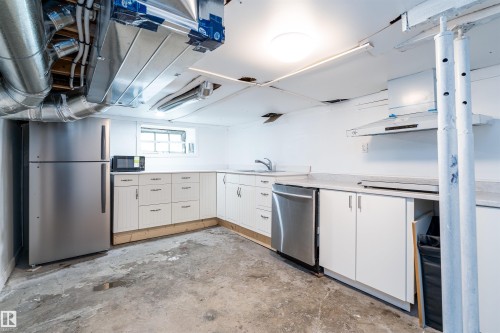 Compact kitchen area featuring white cabinetry, a stainless steel refrigerator, and a built-in dishwasher - 10934 80 Avenue Nw, Edmonton, AB - Indoor