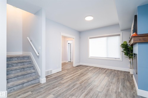 Living area featuring wood-finish flooring, a contemporary fireplace with a wood mantle, and a large window with roller shades - 10934 80 Avenue Nw, Edmonton, AB - Indoor Photo Showing Other Room