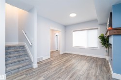 Living area featuring wood-finish flooring, a contemporary fireplace with a wood mantle, and a large window with roller shades - 