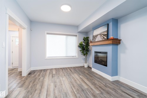 Living area featuring wood-finish flooring, a contemporary electric fireplace with a wood mantle, a large window, and recessed ceiling lighting - 10934 80 Avenue Nw, Edmonton, AB - Indoor With Fireplace