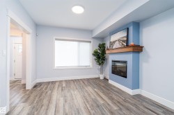 Living area featuring wood-finish flooring, a contemporary electric fireplace with a wood mantle, a large window, and recessed ceiling lighting - 