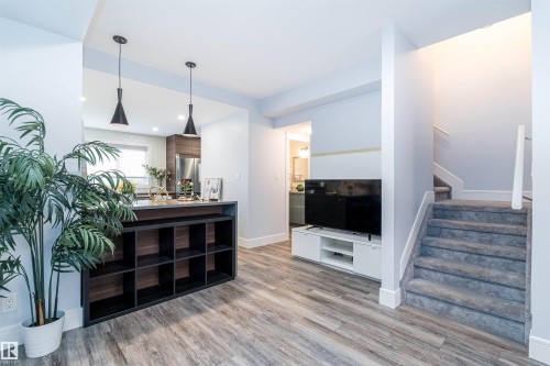 Open-concept living area featuring wood-finish flooring, a built-in shelving unit, and a carpeted staircase with white railings - 10934 80 Avenue Nw, Edmonton, AB - Indoor