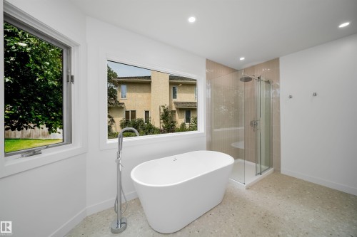Freestanding soaking tub with floor-mounted faucet, glass-enclosed shower with tiled surround, recessed lighting, and dual windows - #A 12 Invermere Pl, St. Albert, AB - Indoor Photo Showing Bathroom