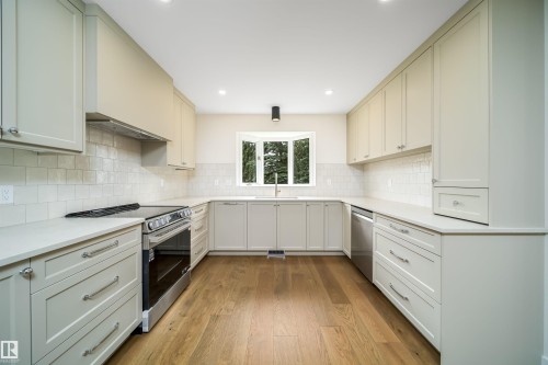 Galley kitchen featuring light-toned cabinetry, light countertops, subway tile backsplash, and wood-finish flooring - #A 12 Invermere Pl, St. Albert, AB - Indoor Photo Showing Kitchen With Upgraded Kitchen