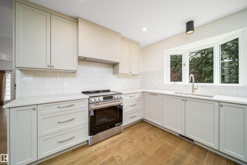 Well-appointed kitchen featuring light-toned cabinetry, a stainless steel range, a subway tile backsplash, light-toned countertops, and wood-finish flooring - #A 12 Invermere Pl, St. Albert, AB - Indoor Photo Showing Kitchen
