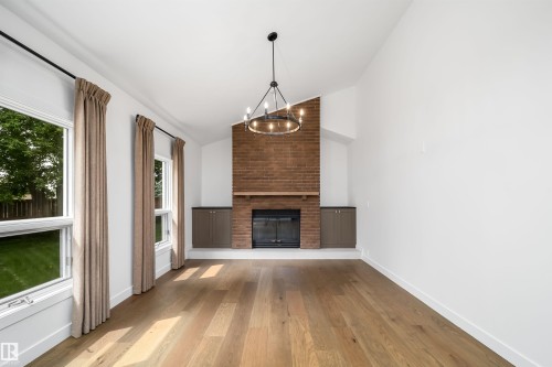 Vaulted ceiling with an overhead chandelier, brick-finish fireplace with a wood mantle, built-in cabinetry, and wood-finish flooring - #A 12 Invermere Pl, St. Albert, AB - Indoor Photo Showing Living Room With Fireplace