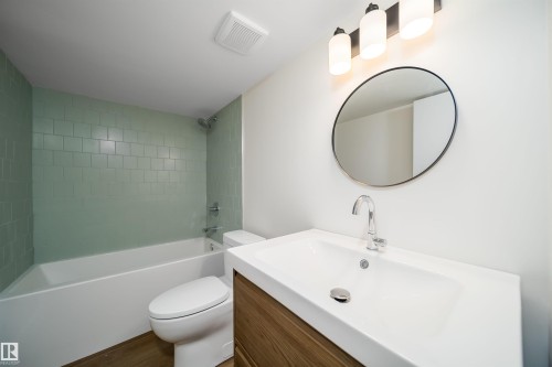 Modern bathroom featuring a circular framed mirror with matte black trim, white rectangular vessel sink with chrome wall-mounted faucet, and wood-finish vanity cabinetry - #A 12 Invermere Pl, St. Albert, AB - Indoor Photo Showing Bathroom