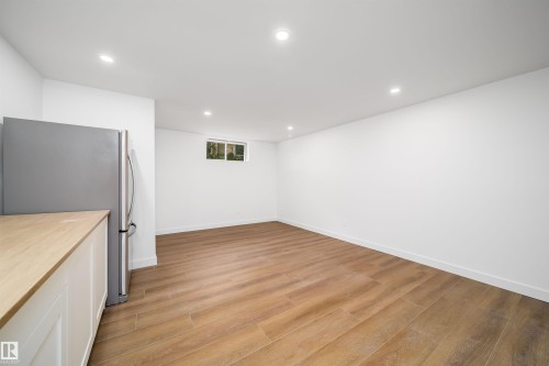 Recessed lighting, wood-finish flooring, white walls, white cabinetry, and stainless steel refrigerator - #A 12 Invermere Pl, St. Albert, AB - Indoor Photo Showing Other Room