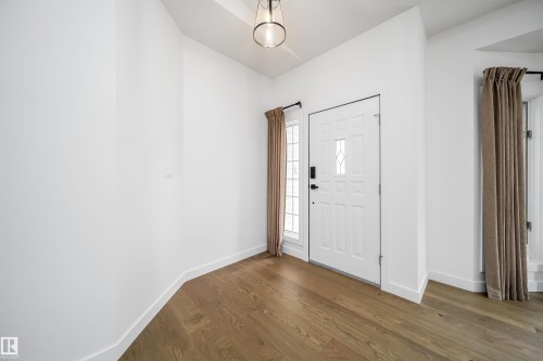 Wood-finish flooring, white paneled door with decorative glass inserts, and a modern pendant light fixture - #A 12 Invermere Pl, St. Albert, AB - Indoor Photo Showing Other Room