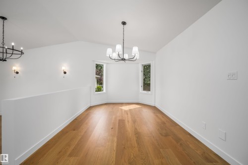 Hardwood-style flooring in a white-walled space with a bay window, accented by a black chandelier and sconces - #A 12 Invermere Pl, St. Albert, AB - Indoor Photo Showing Other Room