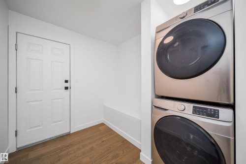 Wood-finish flooring, white paneled door with matte black hardware, and stacked laundry appliances - #A 12 Invermere Pl, St. Albert, AB - Indoor Photo Showing Laundry Room