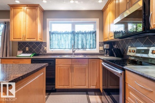 Kitchen featuring wood cabinetry, dark countertops, a tile backsplash, and a stainless steel oven with an overhead microwave - 14514 101 Avenue Nw, Edmonton, AB - Indoor Photo Showing Kitchen With Double Sink