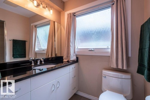 Bathroom featuring a dark granite countertop and white cabinetry, a large mirror, a window with privacy glass, and a toilet - 14514 101 Avenue Nw, Edmonton, AB - Indoor Photo Showing Bathroom