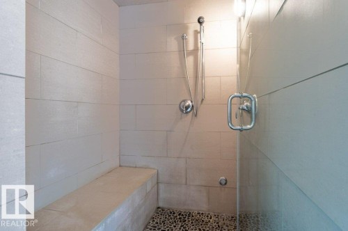 Walk-in Steam/shower featuring light-toned rectangular wall tiles, a built-in bench, pebble-style flooring, a handheld shower fixture, and a clear glass enclosure with a polished chrome handle - 14514 101 Avenue Nw, Edmonton, AB - Indoor Photo Showing Bathroom
