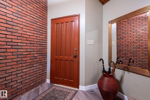 Entryway featuring a paneled wood door, wood-finish flooring, and a decorative brick accent wall - 14514 101 Avenue Nw, Edmonton, AB - Indoor Photo Showing Other Room