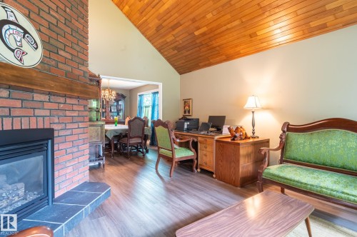 Wood-finish flooring throughout, featuring a brick fireplace with a dark stone hearth and a contrasting wood mantel - 14514 101 Avenue Nw, Edmonton, AB - Indoor With Fireplace