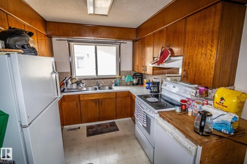 U-shaped kitchen featuring wood cabinetry, white countertops, tile backsplash, and a double basin stainless steel sink with a window above - 4322 49 Ave, St. Paul Town, AB - Indoor Photo Showing Kitchen With Double Sink