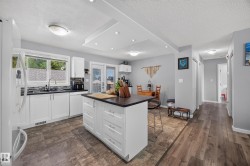 Modern kitchen featuring white cabinetry with a large center island, wood-finish flooring throughout, stainless steel appliances, and abundant natural light from multi-pane windows - 