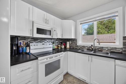 White cabinetry with brushed nickel hardware, dark countertops, tiled backsplash, dual basin stainless steel sink, and a built-in microwave - 156 Clareview Road Nw, Edmonton, AB - Indoor Photo Showing Kitchen With Double Sink