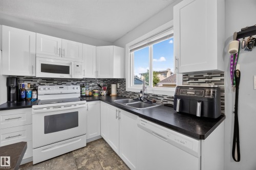 White cabinetry, dark countertops, a tiled backsplash, and stainless steel sink - 156 Clareview Road Nw, Edmonton, AB - Indoor Photo Showing Kitchen With Double Sink