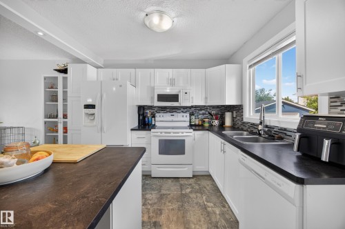 White cabinetry with brushed nickel hardware, dark countertops, dual basin stainless steel sink, tiled backsplash, and wood-finish flooring - 156 Clareview Road Nw, Edmonton, AB - Indoor Photo Showing Kitchen With Double Sink