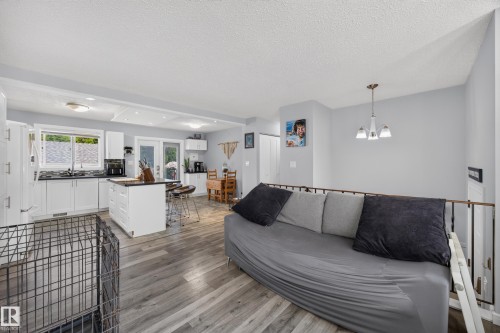 Open-concept living space featuring wood-finish flooring, white kitchen cabinetry, a kitchen island with seating, a dining area, and a metal railing - 156 Clareview Road Nw, Edmonton, AB - Indoor Photo Showing Other Room