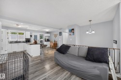 Open-concept living space featuring wood-finish flooring, white kitchen cabinetry, a kitchen island with seating, a dining area, and a metal railing - 
