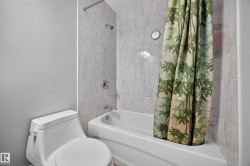 White ceramic toilet and bathtub with a tiled shower surround featuring a chrome shower head and faucet - 