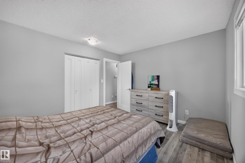 Spacious secondary bedroom featuring wood-finish flooring, a six-drawer dresser with ample storage, double closets with bifold doors, and abundant natural light from a large window - 156 Clareview Road Nw, Edmonton, AB - Indoor Photo Showing Bedroom