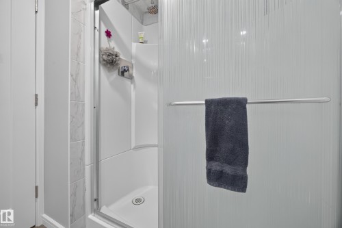 Shower enclosure featuring a built-in shelf, marble-look tile, and a textured privacy glass panel - 156 Clareview Road Nw, Edmonton, AB - Indoor Photo Showing Bathroom