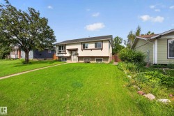 Split-level residence featuring a bay window, concrete walkway, and a mature tree - 